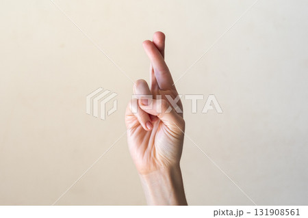A close-up of a human hand with fingers crossed, symbolizing hope or a wish. The hand is light-skinned with neatly manicured nails against a neutral background. 131908561