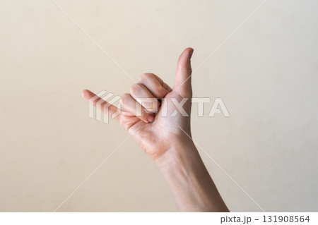 A close-up of a human hand making a shaka sign against a neutral background. The hand is of a light skin tone with well-groomed fingers. A close-up of a human hand making a shaka sign against a neutral background. The hand is of a light skin tone with well-groomed fingers. 131908564