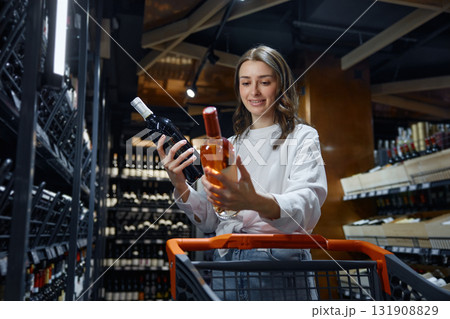 A woman is holding a bottle of wine inside a grocery store A woman is holding a bottle of wine inside a grocery store 131908829
