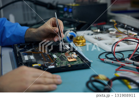 A man works on his laptop while using a soldering iron 131908911
