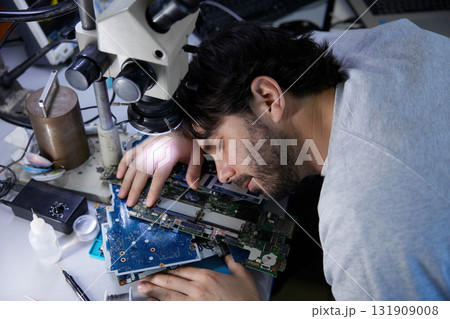 A tired man is sleeping on a large bunch of various electronic components in a lab 131909008