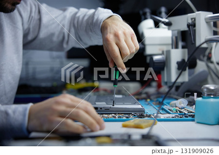 A technician is carefully repairing a circuit board with precision tools in a workshop 131909026