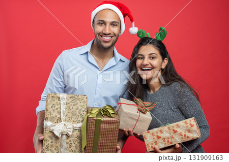 Cheerful couple holding gift boxes during Xmas celebration with festive hats and tinsel Cheerful couple holding gift boxes during Xmas celebration with festive hats and tinsel 131909163