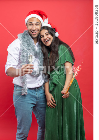 Happy couple in Santa hats with champagne glasses and holding sparkle celebrating Xmas together Happy couple in Santa hats with champagne glasses and holding sparkle celebrating Xmas together 131909258