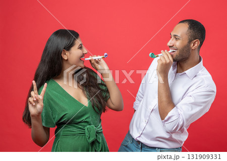 Happy couple celebrating holiday on party blowing in whistle isolated over red background Happy couple celebrating holiday on party blowing in whistle isolated over red background 131909331