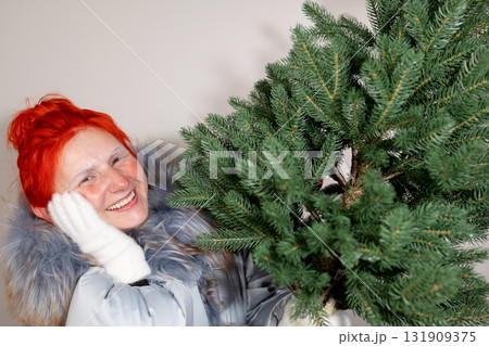 Frozen Woman Smiles Holding Small Christmas Tree in Winter Coat and Gloves Frozen Woman Smiles Holding Small Christmas Tree in Winter Coat and Gloves 131909375