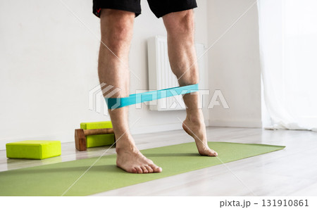 Sporty Man Exercises With A Resistance Rubber Band At Home For Strong Legs Sporty Man Exercises With A Resistance Rubber Band At Home For Strong Legs 131910861