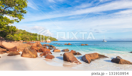 Sunlit tropical beach scene with smooth white sand, warm rocks and turquoise sea 131910954