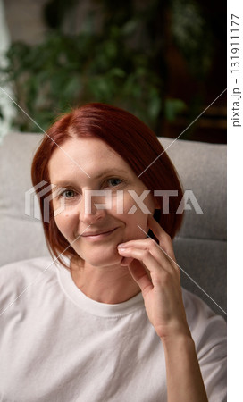 Portrait of calm red-haired woman smiling softly while relaxing indoors in natural light Portrait of calm red-haired woman smiling softly while relaxing indoors in natural light 131911177
