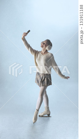 Cheerful woman ice skater taking selfie on frozen surface in cozy winter outfit 131911188