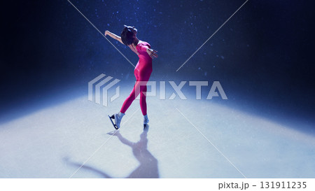 Female ice skater in elegant pose on rink illuminated by spotlight expressing freedom and grace 131911235
