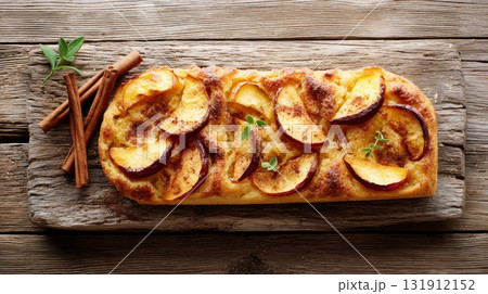 Delicious focaccia bread topped with caramelized apple slices rests on a rustic wooden surface, perfect for autumn celebrations 131912152