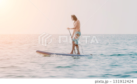 Man Paddleboarding Ocean Sunset - A man enjoys paddleboarding on a calm ocean during a beautiful sunset. Man Paddleboarding Ocean Sunset - A man enjoys paddleboarding on a calm ocean during a beautiful sunset. 131912424