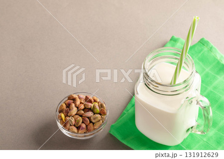 Pistachios in a bowl beside glass of milk with straw on green napkin Copy space for text 131912629