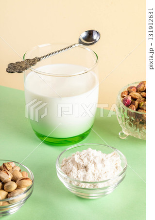 Alternative plant based milk. Pistachios milk in glass with spoon, pistachios, nutty flour on green 131912631