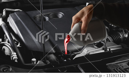 Mechanic hand pouring red transmission fluid into car engine under hood close up Mechanic hand pouring red transmission fluid into car engine under hood close up 131913123