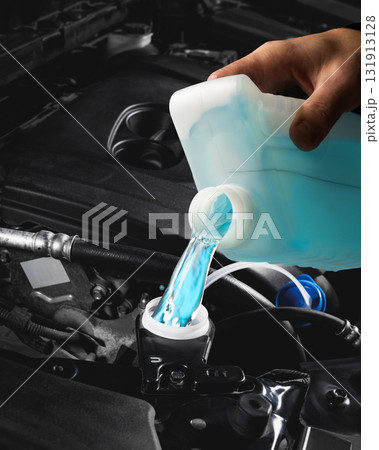 Blue windshield washer fluid being poured into car reservoir under hood close up 131913128