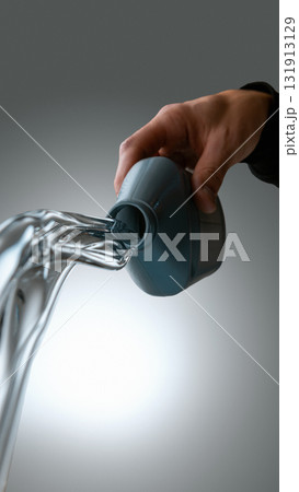 Hand pouring transparent automotive fluid from gray bottle on neutral background Hand pouring transparent automotive fluid from gray bottle on neutral background 131913129