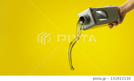 Stream of golden motor oil pouring from plastic container on yellow background 131913130