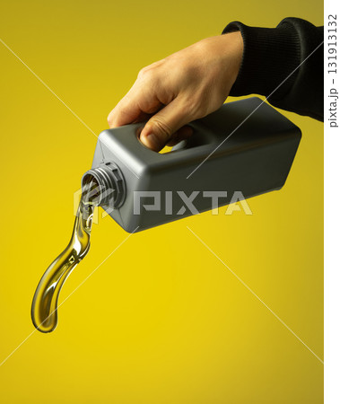 Mechanic hand holding gray container pouring motor oil with soft reflection on yellow background 131913132