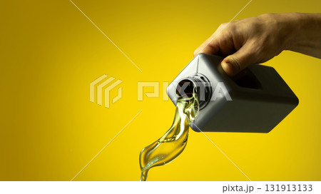 Hand pouring golden engine oil from container with splash motion on yellow backdrop Hand pouring golden engine oil from container with splash motion on yellow backdrop 131913133