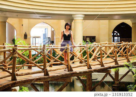 A pretty female tourist in light clothing stands on a decorative bridge inside a hotel A pretty female tourist in light clothing stands on a decorative bridge inside a hotel 131913352