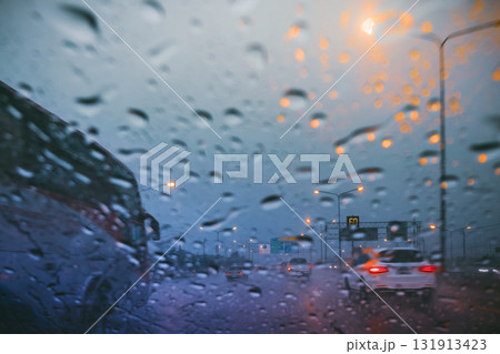Driving on a rain-slicked highway at twilight, viewed through a wet car windshield with blurred traffic and orange streetlights 131913423