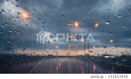 Rainy night drive with water droplets on the car windshield and blurred streetlights in the background Rainy night drive with water droplets on the car windshield and blurred streetlights in the background 131913430