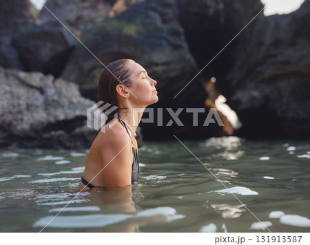 Young woman enjoying serene evening at sea in Krabi, Thailand during sunset. Calm waves, golden light, and peaceful atmosphere highlight tropical beauty and connection with nature. Young woman enjoying serene evening at sea in Krabi, Thailand during sunset. Calm waves, golden light, and peaceful atmosphere highlight tropical beauty and connection with nature. 131913587