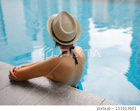 Young asian woman relaxing by pool at Kuala Lumpur hotel with view of surrounding skyscrapers, enjoying leisure time in vibrant urban setting. 131913601