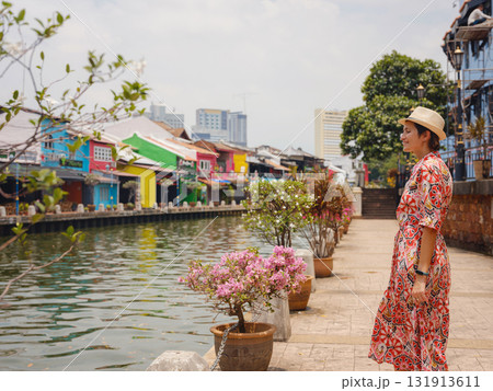 Young woman in ethnic dress and hat exploring the vibrant streets of Malacca, Malaysia. A blend of cultural heritage, colorful architecture, and tropical charm. Perfect travel and lifestyle moments. Young woman in ethnic dress and hat exploring the vibrant streets of Malacca, Malaysia. A blend of cultural heritage, colorful architecture, and tropical charm. Perfect travel and lifestyle moments. 131913611