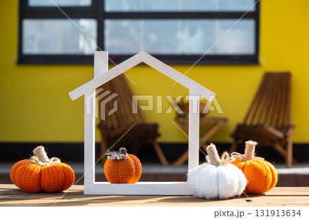 Autumn decor on porch of yellow house outside of pumpkin, lantern, garlands and figure of tiny home and key. Halloween party, autumn mood, Harvest festival, real estate, insurance, mortgage 131913634