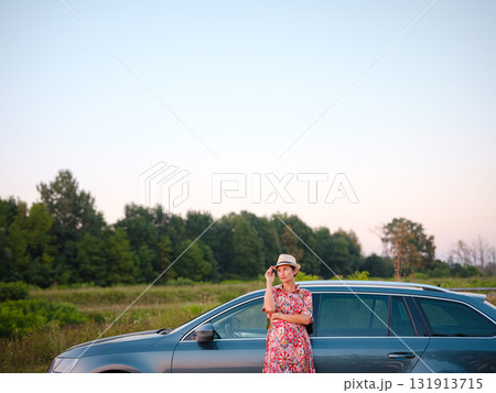 Traveler woman in red ethnic dress and hat drives car through scenic countryside of Croatia in summer. Surrounded by lush fields and forests, she enjoys peaceful and adventurous road trip 131913715