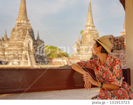 Young female tourist in dress exploring historic park of Ayutthaya, Thailand. Wat Phra Si Sanphet ancient temples and statues, she enjoys peaceful atmosphere and rich cultural heritage. 131913723