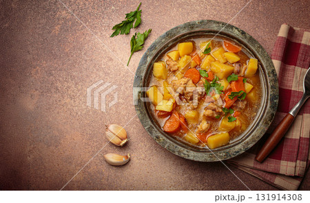 Chicken stew or soup with potatoes and carrots served in rustic bowl with spoon top view on dark brown concrete background, space for text 131914308