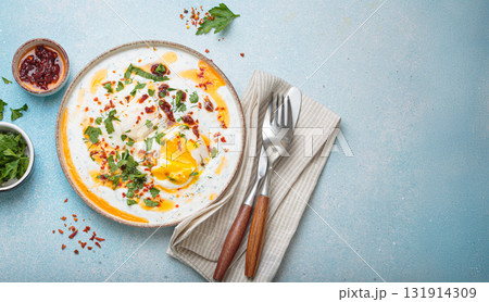 Turkish eggs cilbir, Middle Eastern style breakfast on blue background table top view, space for text Turkish eggs cilbir, Middle Eastern style breakfast on blue background table top view, space for text 131914309
