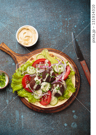 Preparing and cooking falafel wrap on pita on wooden cutting board with hummus top view Preparing and cooking falafel wrap on pita on wooden cutting board with hummus top view 131914310