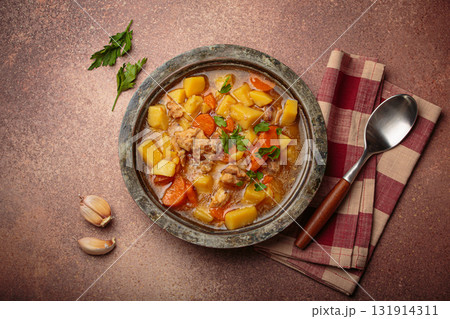 Chicken stew or soup with potatoes and carrots served in rustic bowl with spoon top view on dark brown concrete background 131914311