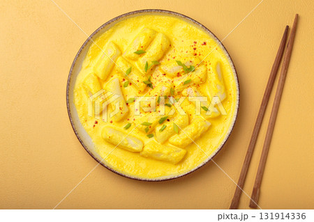 Traditional korean tteokbokki in creamy cheese sauce with garnish, wooden chopsticks on rustic yellow background top view 131914336