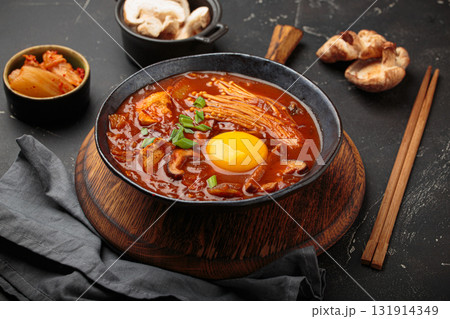 Traditional Korean kimchi jjigae hot soup or stew with egg yolk in black rustic bowl on dark background top view 131914349