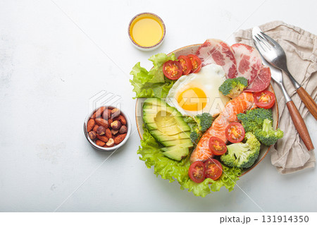 Balanced ketogenic diet meal with salmon, avocado, egg, bacon and vegetables on plate with cutlery top view on white background, space for text 131914350