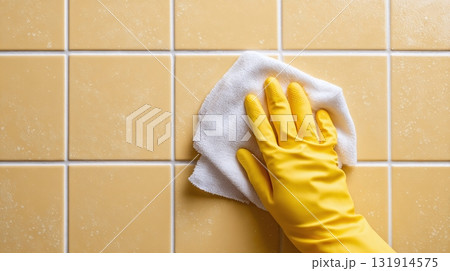 Cleaning Tile with Cloth: A gloved hand wipes yellow tiles with a white cloth, showcasing cleanliness and maintenance in a domestic setting. Cleaning Tile with Cloth: A gloved hand wipes yellow tiles with a white cloth, showcasing cleanliness and maintenance in a domestic setting. 131914575