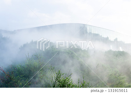 Artificial fog in a modern park with a mirrored wall of a futuristic building in the background 131915011