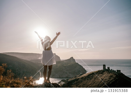 A woman is standing on a hill overlooking a body of water. She is wearing a white dress and she is happy. A woman is standing on a hill overlooking a body of water. She is wearing a white dress and she is happy. 131915388