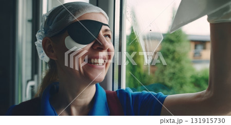 Woman with eyepatch cleaning window, smiling with joy Woman with eyepatch cleaning window, smiling with joy 131915730