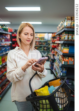 Woman using smartphone for grocery shopping in supermarket Woman using smartphone for grocery shopping in supermarket 131916212