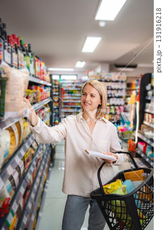 Woman shopping for groceries in supermarket aisle with basket Woman shopping for groceries in supermarket aisle with basket 131916218