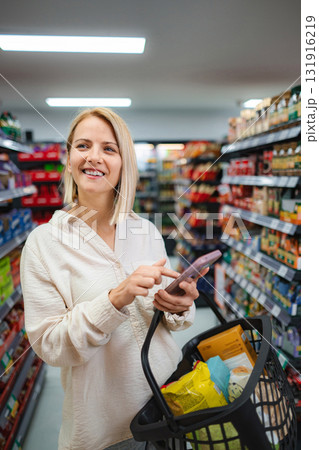 Woman smiling using phone shopping in grocery store Woman smiling using phone shopping in grocery store 131916219