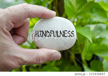Hand holding a white stone with MINDFULNESS text engraved on it, expressing life purpose of awareness and being present 131916647