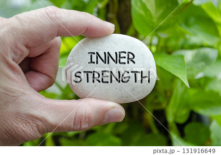 Hand holding a white stone with INNER STRENGTH text engraved on it, representing life purpose of resilience and personal power 131916649